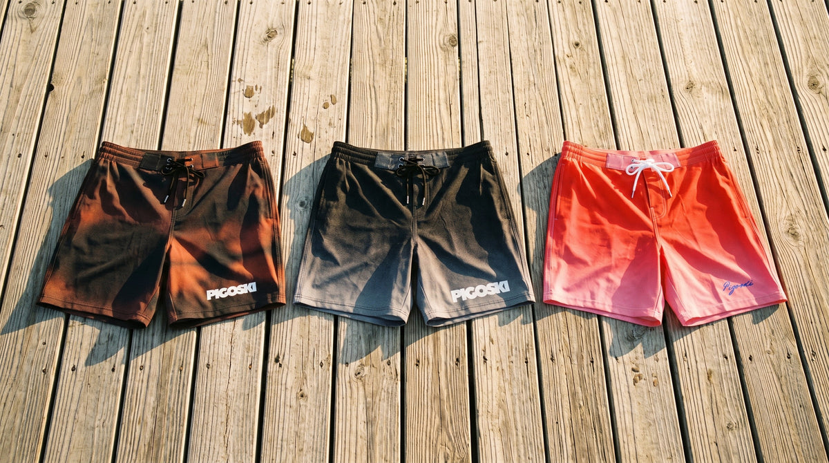 Red Fuse, Mascot and Rose Fuse PIGOSKI board shorts laid on sunlit dock planks — Board Shorts collection banner