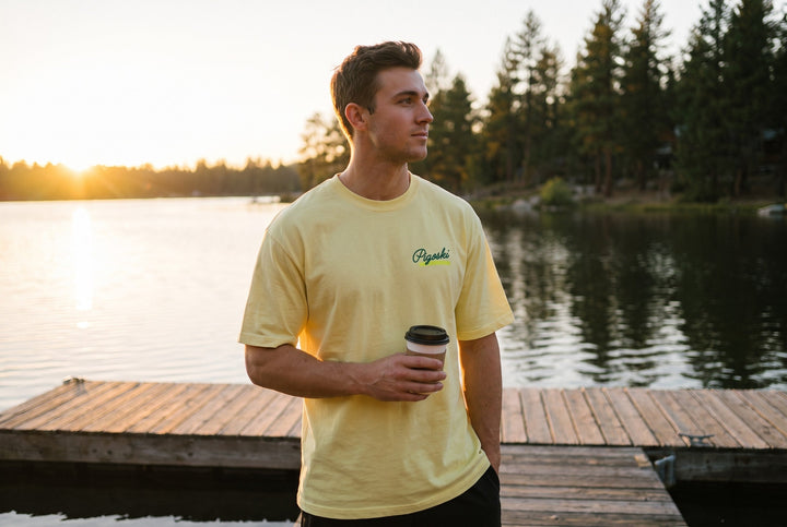 Skier wearing the PIGOSKI Ritual Tee in butter yellow at golden hour on a lake dock