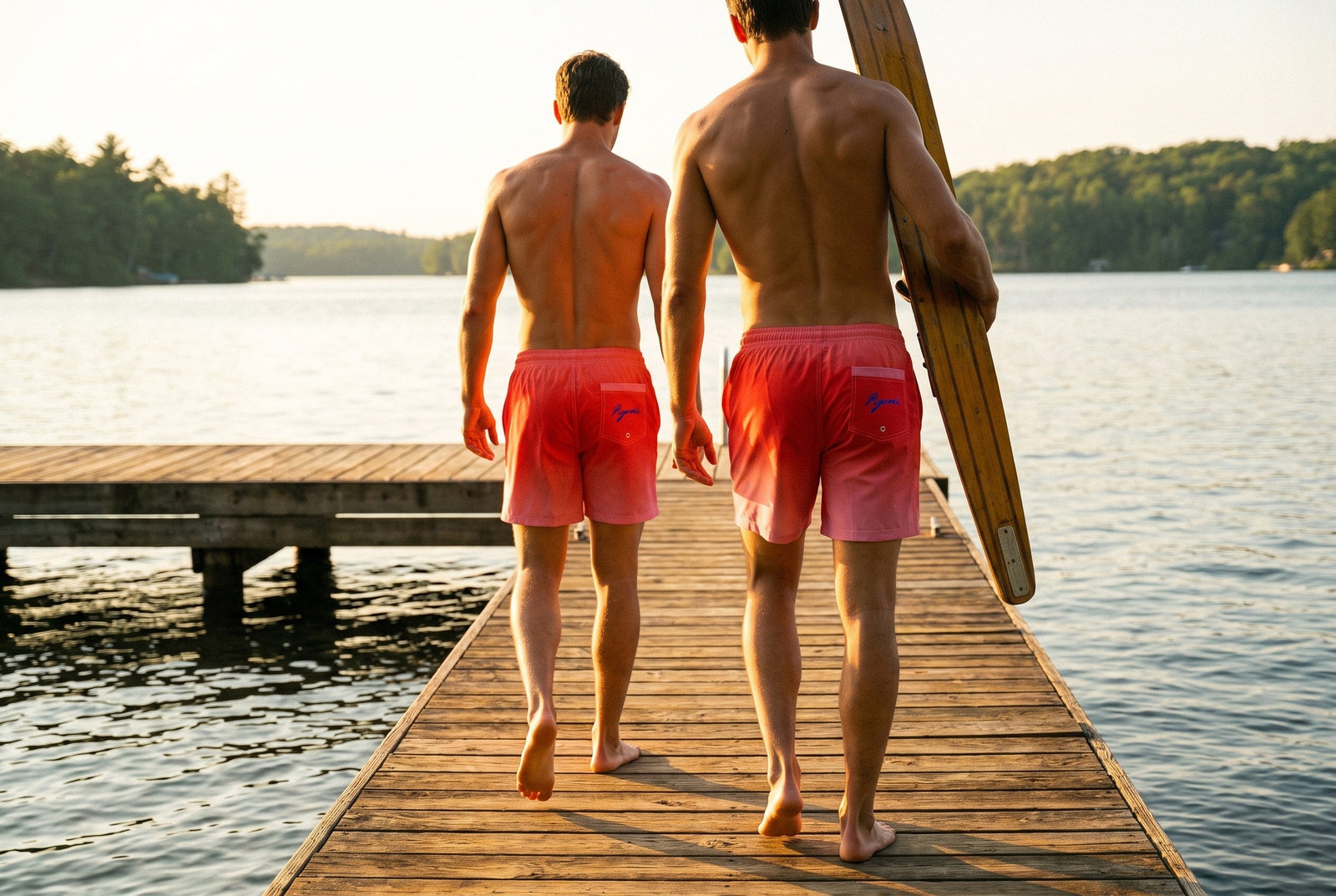 Two skiers walking a lake dock in PIGOSKI Rose Fuse board shorts, carrying a slalom ski